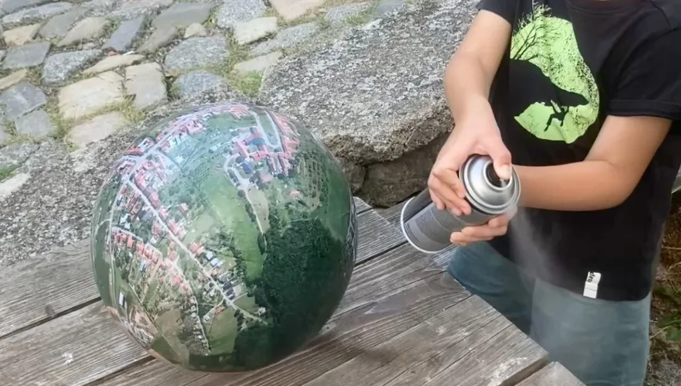 Person spraying clear coat onto a finished aerial-map globe outdoors