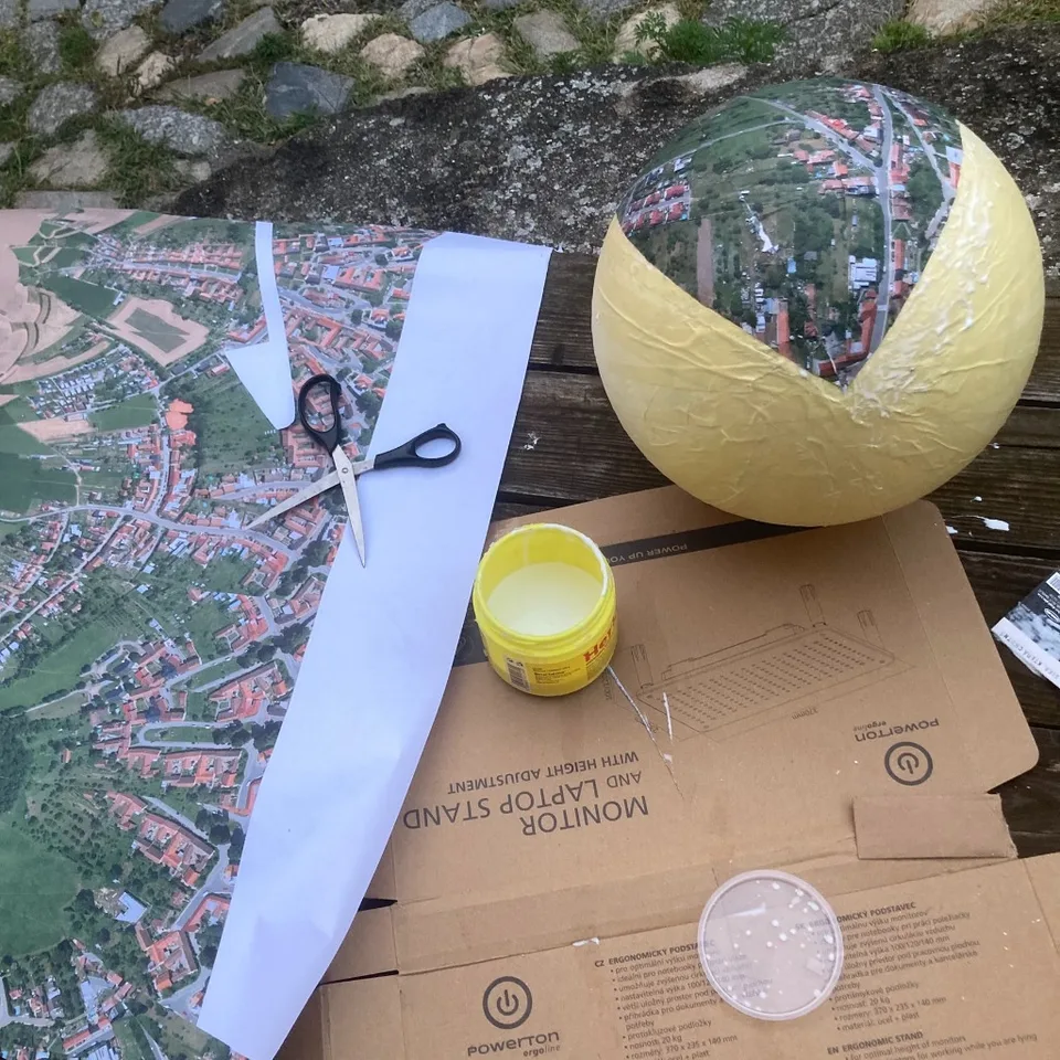 Aerial map stripes being glued onto a papier-mâché globe on a work table